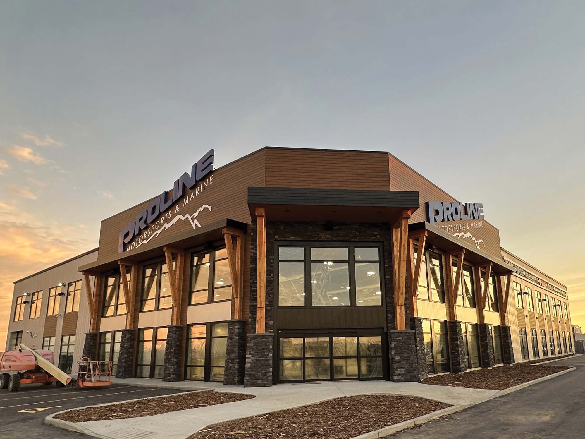 Contemporary commercial office building with warm wood-tone accents, expansive glass frontage and exposed timber detailing illuminated beneath a dramatic sunset sky.